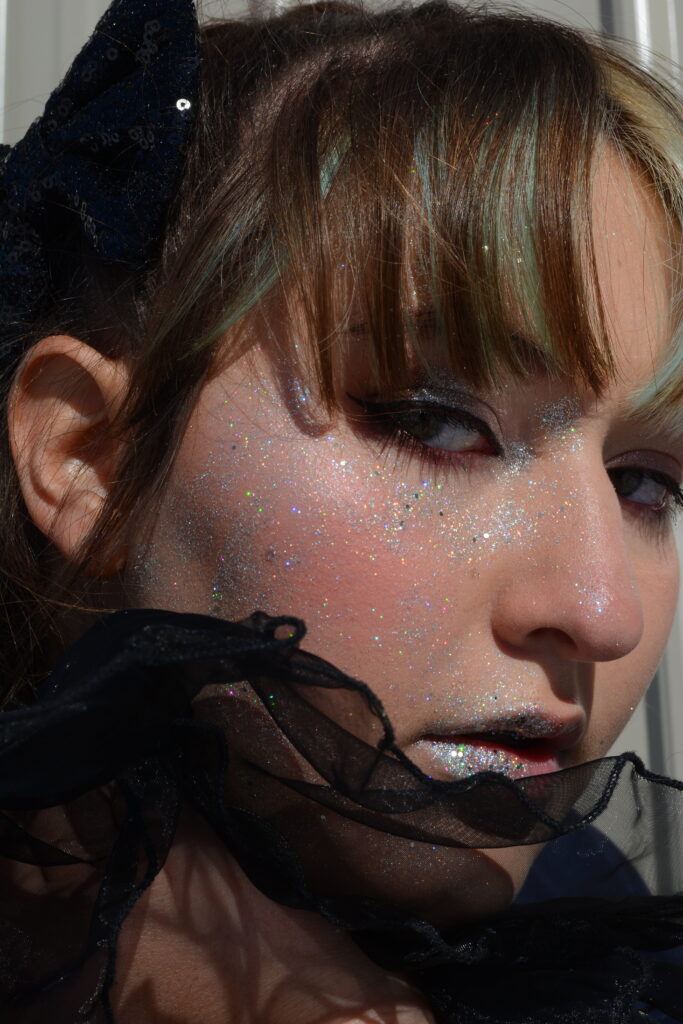 Close up of a woman in black with glitter on her face.